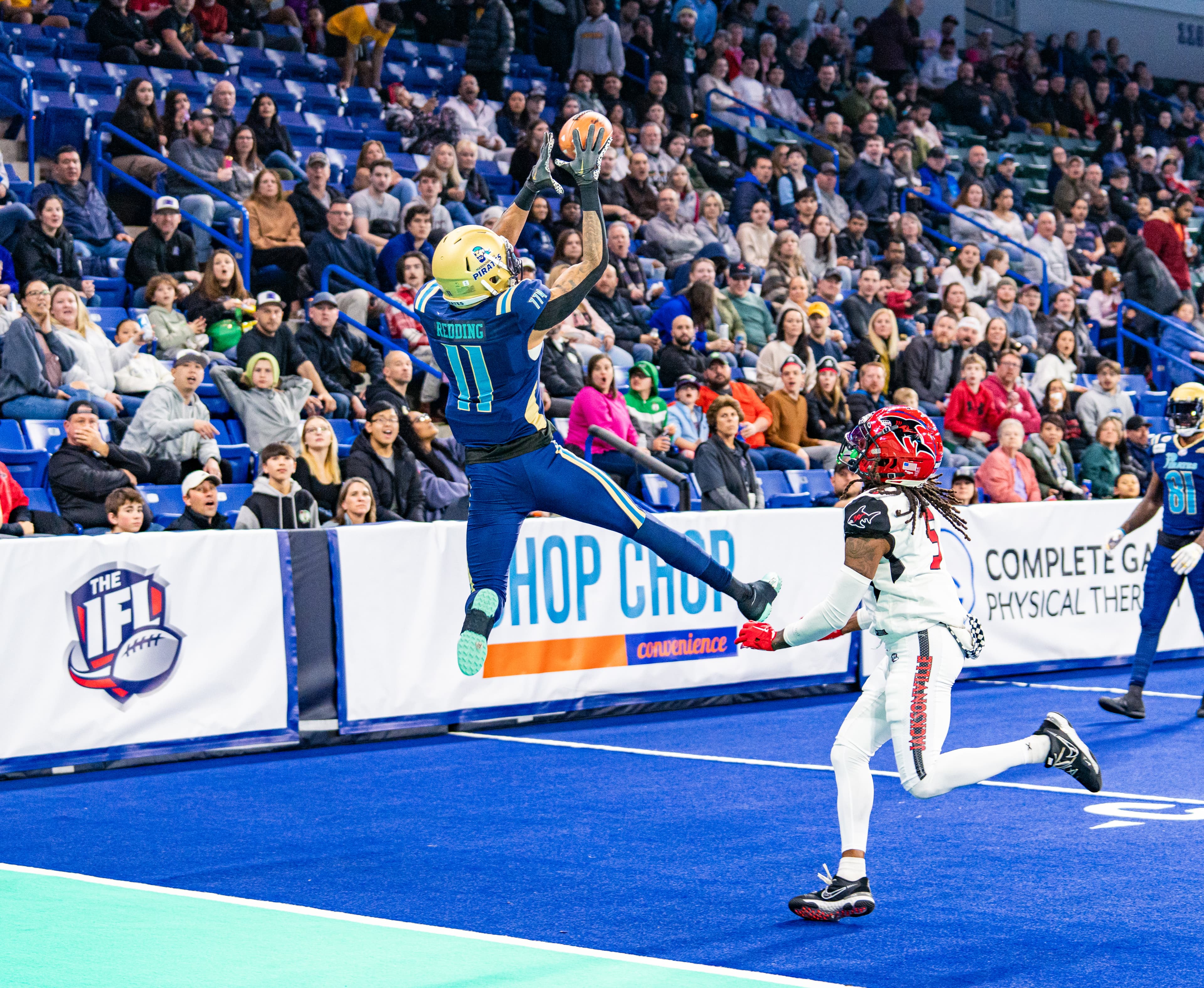 IFL indoor football action — ball carrier sprinting down the field with a defender in pursuit.